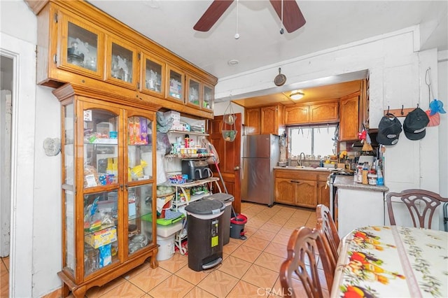 kitchen with ceiling fan, light countertops, freestanding refrigerator, brown cabinetry, and a sink