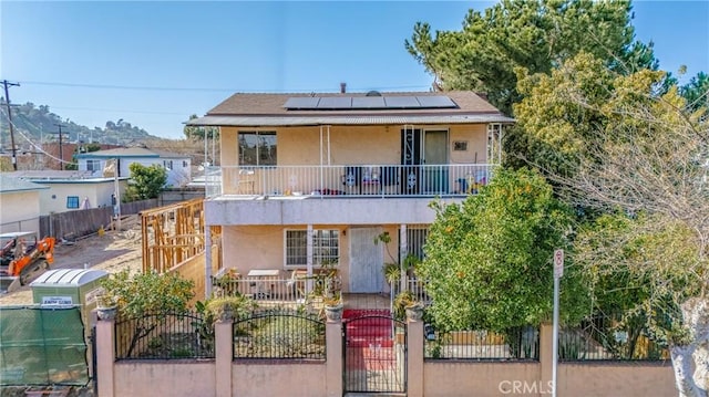 front facade with a fenced front yard, a balcony, solar panels, and stucco siding