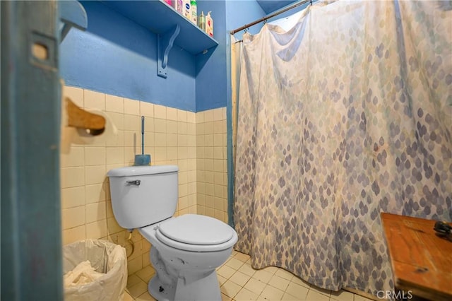 bathroom featuring a shower with curtain, a wainscoted wall, tile patterned flooring, tile walls, and toilet