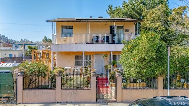 view of property featuring a fenced front yard, a balcony, solar panels, and stucco siding