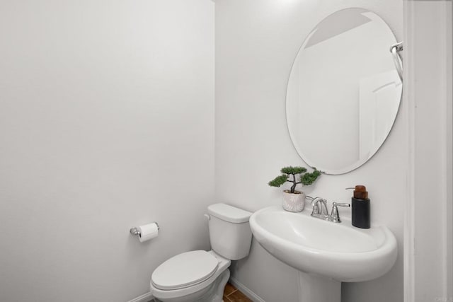 half bath with baseboards, a sink, and toilet