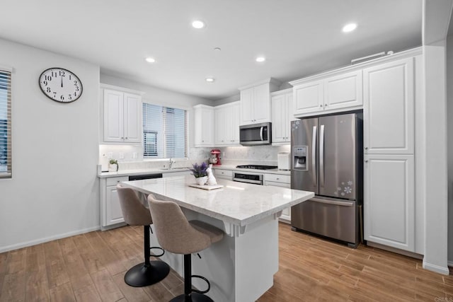 kitchen featuring stainless steel appliances, a sink, white cabinets, a center island, and light wood finished floors