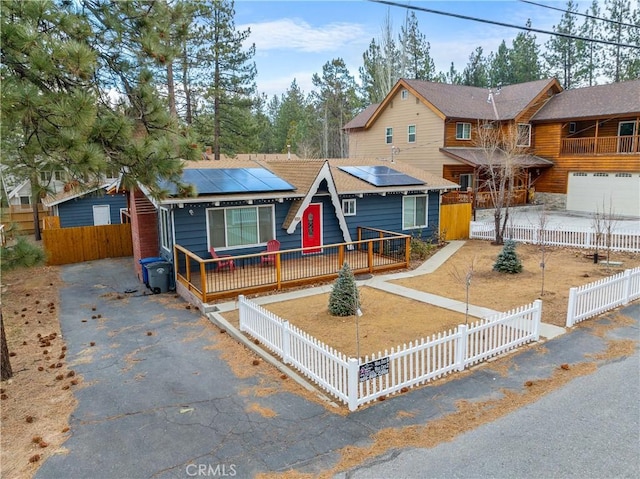 view of front of home with aphalt driveway, a fenced front yard, and roof mounted solar panels