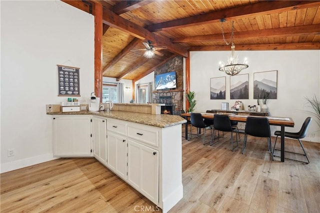 kitchen featuring vaulted ceiling with beams, light wood-style flooring, white cabinetry, a peninsula, and ceiling fan with notable chandelier