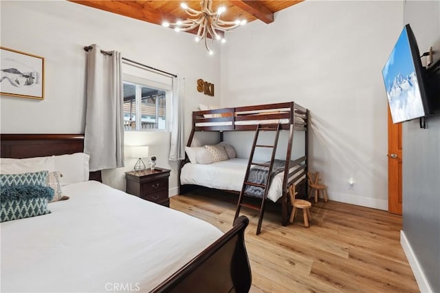 bedroom with baseboards, light wood finished floors, beamed ceiling, and a notable chandelier