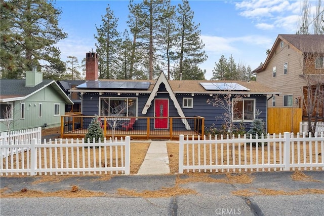 view of front facade featuring a fenced front yard, a chimney, and roof mounted solar panels