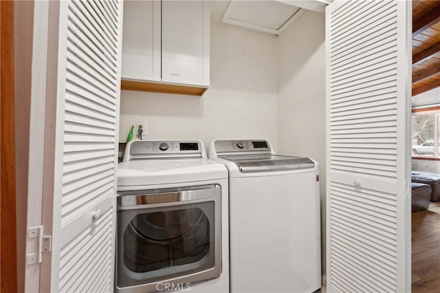 clothes washing area featuring separate washer and dryer, wood finished floors, and cabinet space