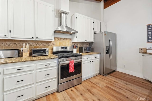 kitchen with stainless steel appliances, tasteful backsplash, light wood-style floors, white cabinets, and wall chimney range hood