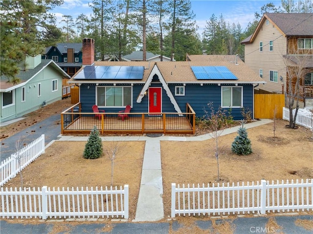 view of front of property featuring roof with shingles, a fenced front yard, a chimney, and roof mounted solar panels