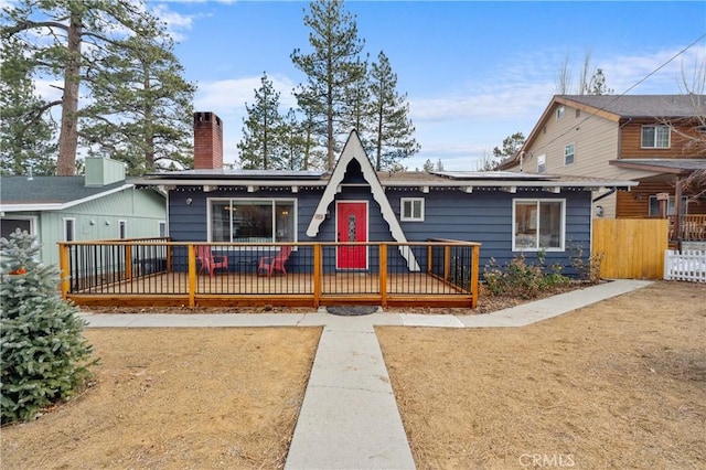 view of front of house featuring a chimney, fence, and roof mounted solar panels