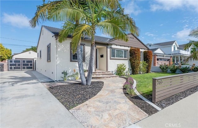 bungalow-style home featuring a gate, a front lawn, and stucco siding