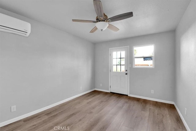 interior space featuring a wall mounted air conditioner, wood finished floors, a ceiling fan, and baseboards