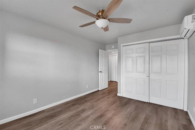 unfurnished bedroom featuring baseboards, a ceiling fan, a wall unit AC, wood finished floors, and a closet