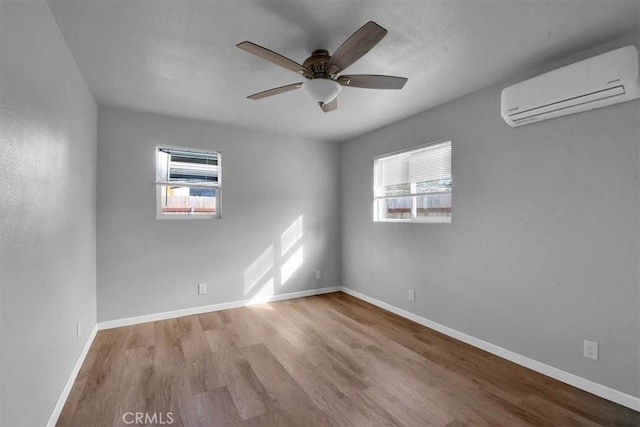 empty room featuring a wall unit AC, plenty of natural light, baseboards, and wood finished floors