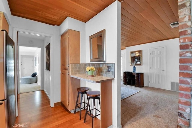 kitchen featuring tasteful backsplash, freestanding refrigerator, wood ceiling, and visible vents