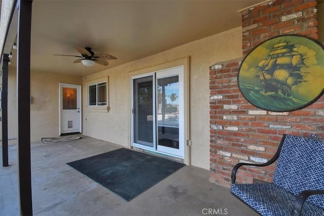 doorway to property with a patio area, brick siding, ceiling fan, and stucco siding