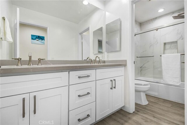 bathroom with toilet, a sink, wood finished floors, combined bath / shower with glass door, and double vanity