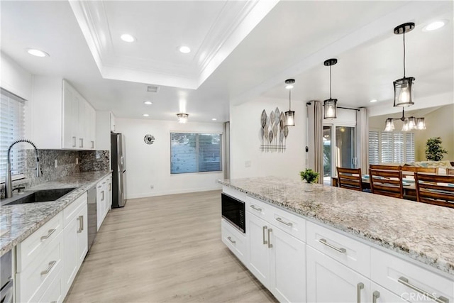 kitchen with light wood finished floors, appliances with stainless steel finishes, a tray ceiling, crown molding, and a sink