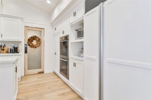 kitchen with tasteful backsplash, light countertops, double oven, white cabinets, and light wood-type flooring