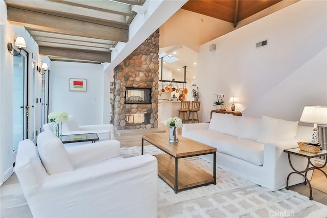 living area with visible vents, beamed ceiling, and a stone fireplace