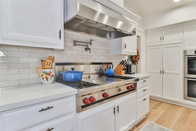 kitchen with wall chimney exhaust hood, light wood-type flooring, light countertops, and stainless steel appliances