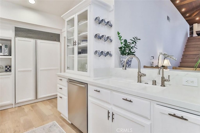 kitchen with paneled built in refrigerator, a sink, dishwasher, light wood finished floors, and glass insert cabinets