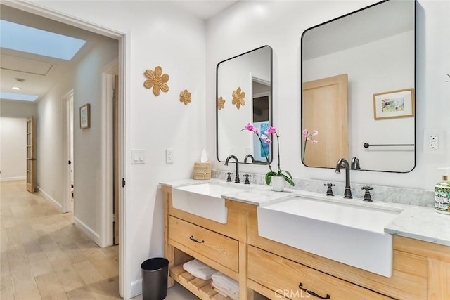 full bathroom with wood finished floors, a sink, baseboards, and double vanity