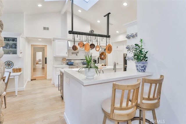 kitchen with a skylight, visible vents, light wood-style floors, white cabinets, and backsplash