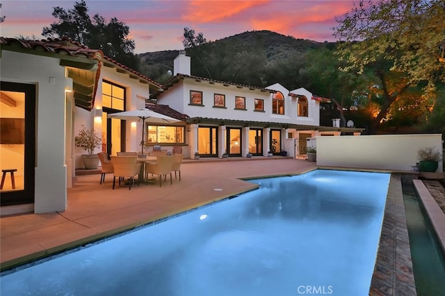 rear view of property featuring stucco siding, a patio area, a mountain view, fence, and an outdoor pool