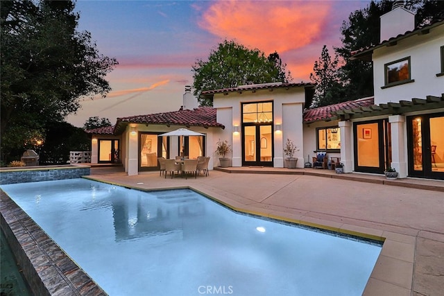 pool at dusk featuring french doors, a patio area, and an outdoor pool