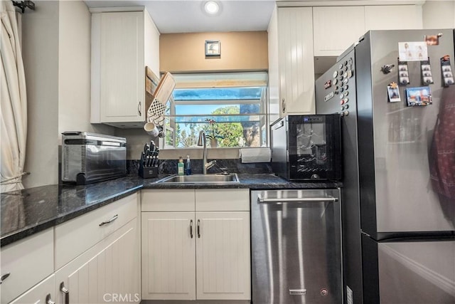 kitchen with appliances with stainless steel finishes, dark stone counters, white cabinets, and a sink