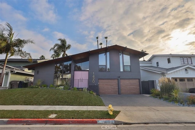 view of front facade with an attached garage, a front lawn, decorative driveway, and stucco siding