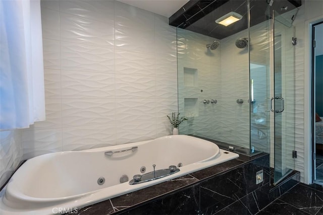 bathroom featuring a tub with jets, a stall shower, and tile walls