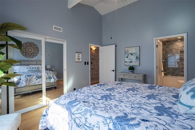 bedroom featuring high vaulted ceiling, ensuite bath, wood finished floors, visible vents, and two closets