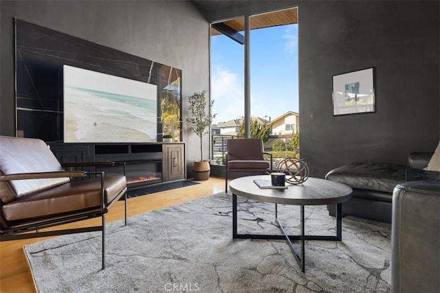 interior space with a high ceiling, a wall of windows, wood finished floors, and a glass covered fireplace