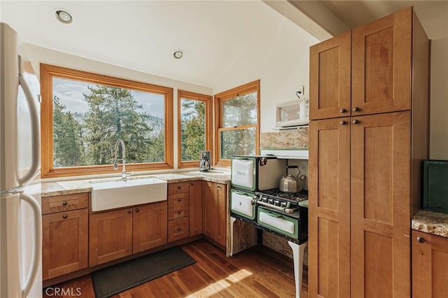 kitchen with white appliances, brown cabinetry, vaulted ceiling, light countertops, and a sink