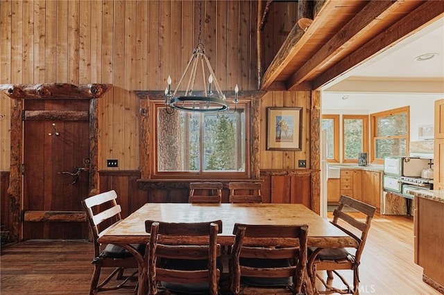 dining area with light wood finished floors, wooden walls, and beamed ceiling