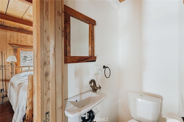 half bathroom featuring beam ceiling, a sink, toilet, and wooden walls