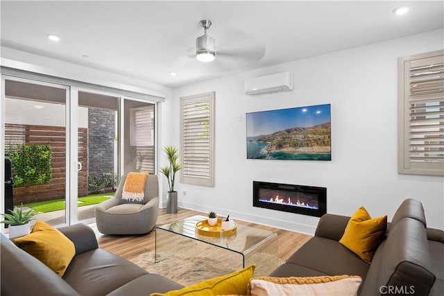 living area featuring recessed lighting, wood finished floors, a ceiling fan, an AC wall unit, and a glass covered fireplace