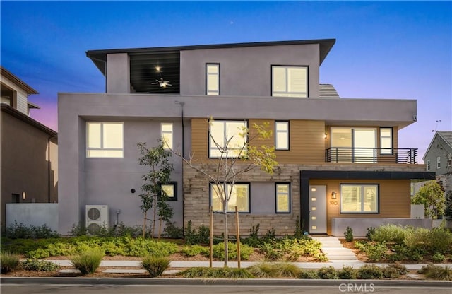 modern home with a balcony, stone siding, and stucco siding