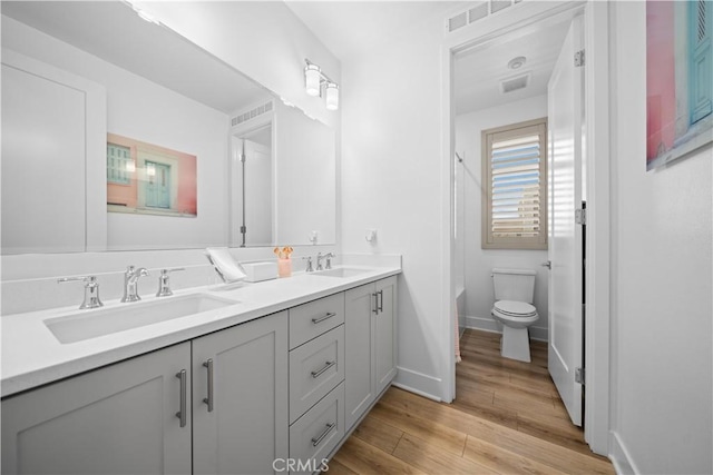 bathroom featuring double vanity, wood finished floors, a sink, and toilet