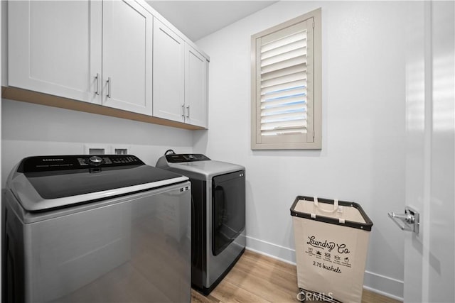 clothes washing area with light wood finished floors, washer and clothes dryer, cabinet space, and baseboards