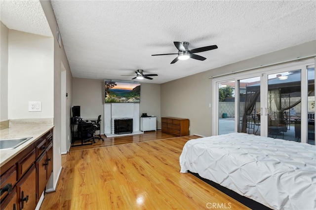 bedroom featuring light wood-style flooring, a fireplace with raised hearth, a sink, a textured ceiling, and access to outside