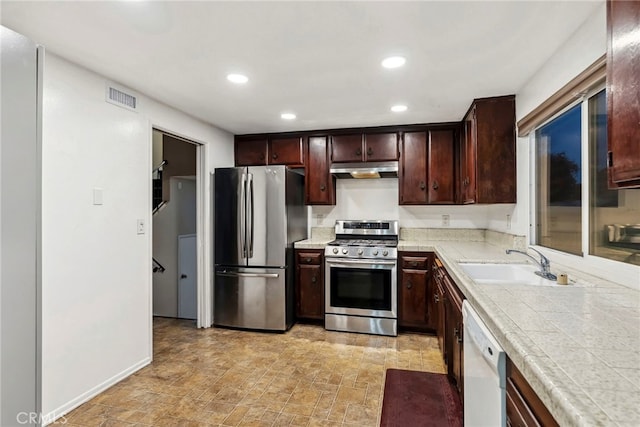 kitchen featuring visible vents, stone finish floor, a sink, under cabinet range hood, and stainless steel appliances