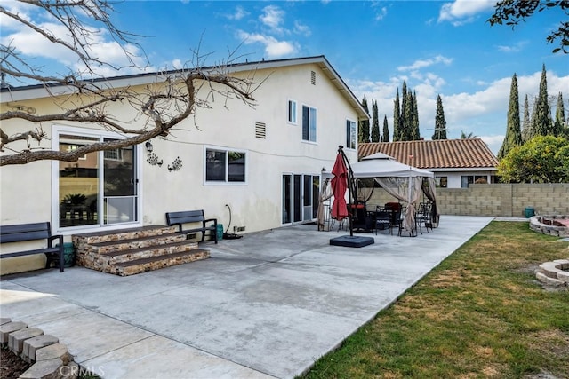 rear view of property featuring fence, entry steps, a gazebo, stucco siding, and a patio