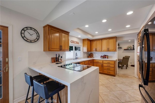 kitchen featuring a kitchen breakfast bar, light countertops, a peninsula, and black appliances