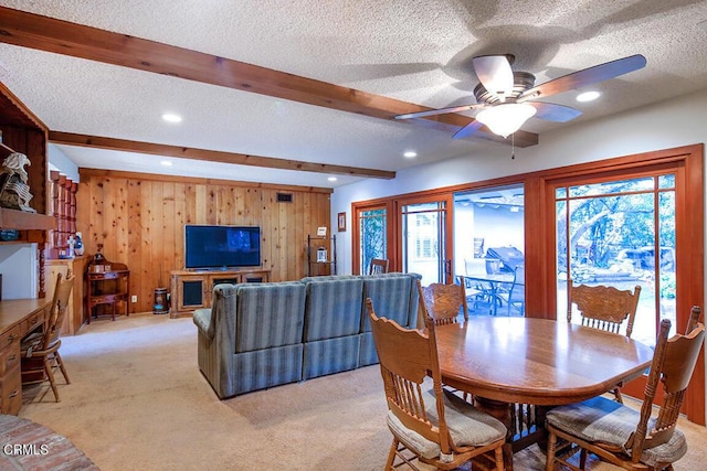 dining space with light carpet, a textured ceiling, beam ceiling, and wooden walls