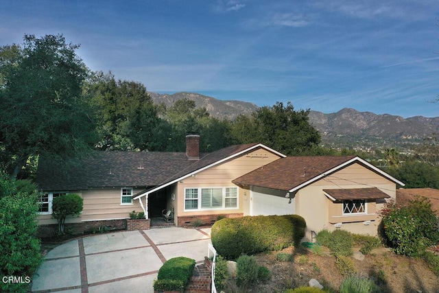 ranch-style home featuring roof with shingles, a mountain view, a chimney, and an attached garage