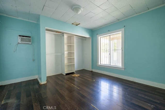 unfurnished bedroom featuring a wall mounted AC, dark wood-style floors, a closet, crown molding, and baseboards