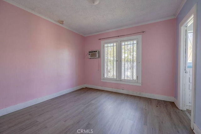 empty room with a wall mounted air conditioner, ornamental molding, a textured ceiling, wood finished floors, and baseboards